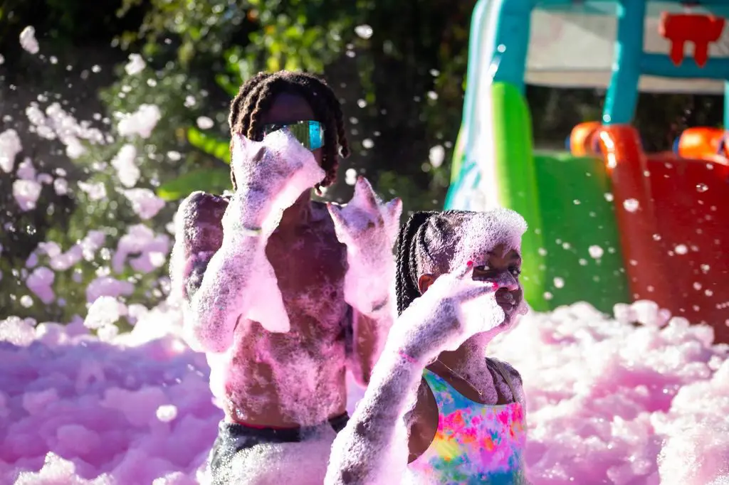 Two people in a foam pit with pink and purple powder.